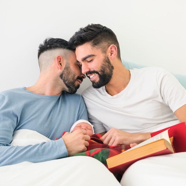 Romántica pareja gay joven sentada en la cama con su bebé