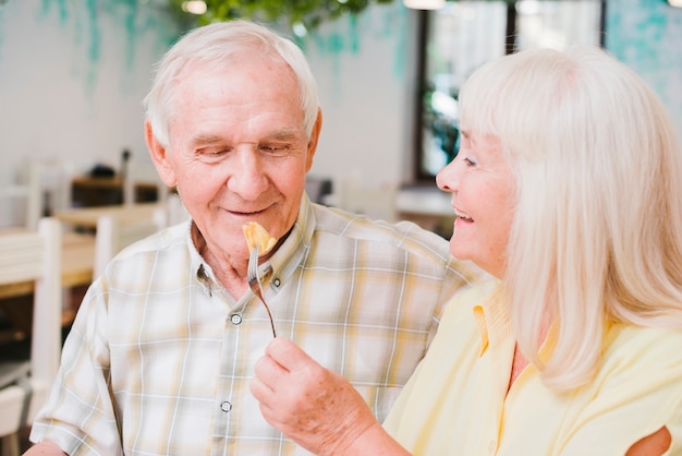 Romántica pareja senior sentado en la cafetería y disfrutando de pastel