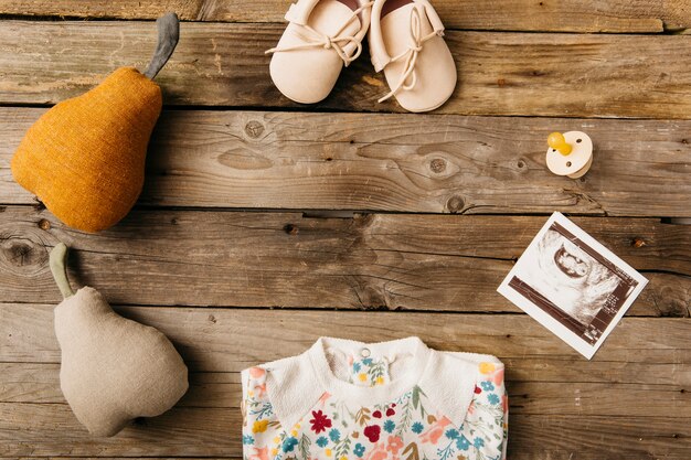 Ropa de bebé; Zapatos; chupete; Imagen de ultrasonido y pera rellena en mesa de madera.