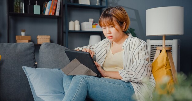 Ropa casual de dama asiática independiente con aprendizaje en línea de tableta en la sala de estar de la casa