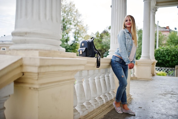 Ropa de chica rubia en jeans con mochila posada contra casa vintage