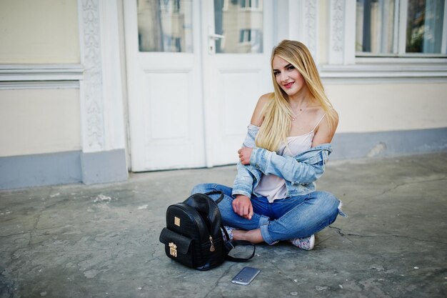 Ropa de chica rubia en jeans con mochila posada contra la puerta vieja