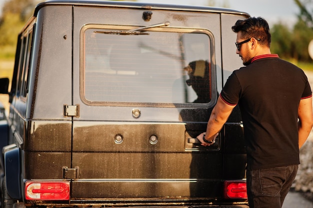 Ropa de hombre asiático en todo negro posado cerca de la puerta trasera abierta del coche suv