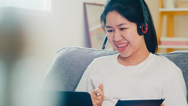 Ropa informal de mujer de negocios independiente asiática usando una videoconferencia de llamada de trabajo portátil con el cliente en el lugar de trabajo en la sala de estar desde casa cuando el distanciamiento social se queda en casa y el tiempo de cuarentena.