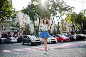 Foto gratuita ropa de niña con estilo rizado en blusa de falda de jeans azules y gafas posadas en la calle de la ciudad con una taza de café