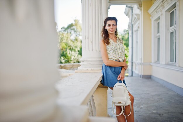 Ropa de niña con estilo rizado en blusa de falda de jeans azules posada cerca de la antigua casa vintage