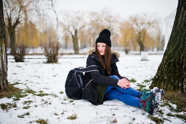 Ropa de niña en jeans largos de sudadera verde y sombreros negros con mochila en el día de invierno