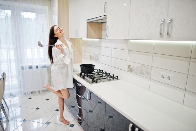 Ropa de niña morena en camisa y ropa interior cocinando en la cocina blanca