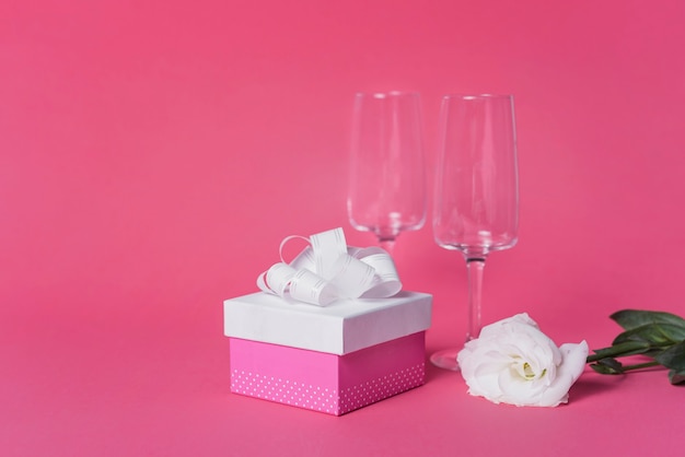 Rosa blanca; caja de regalo y copas de champán flauta sobre fondo rosa