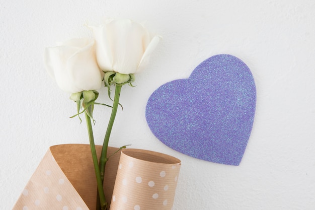 Rosa flores con corazón de papel en mesa