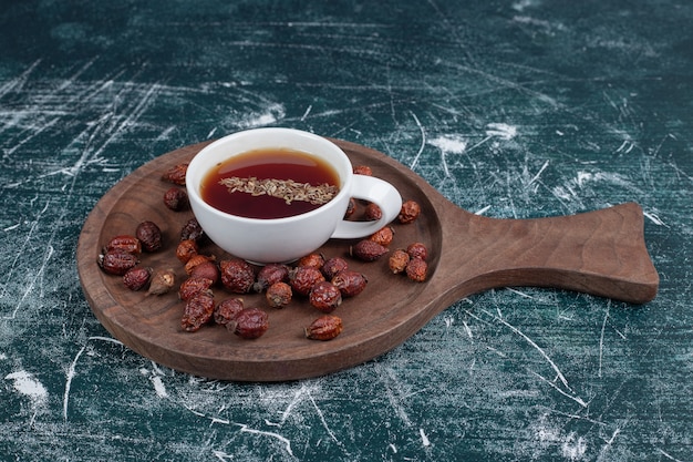 Rosa mosqueta seca y taza de té sobre tabla de madera. Foto de alta calidad