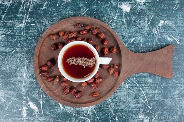 Foto gratuita rosa mosqueta seca y taza de té sobre tabla de madera.