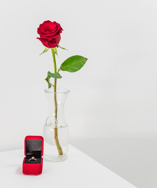 Rosa roja fresca en florero y caja actual con anillo en mesa