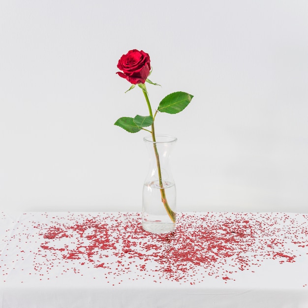 Foto gratuita rosa roja fresca en florero entre confeti en mesa