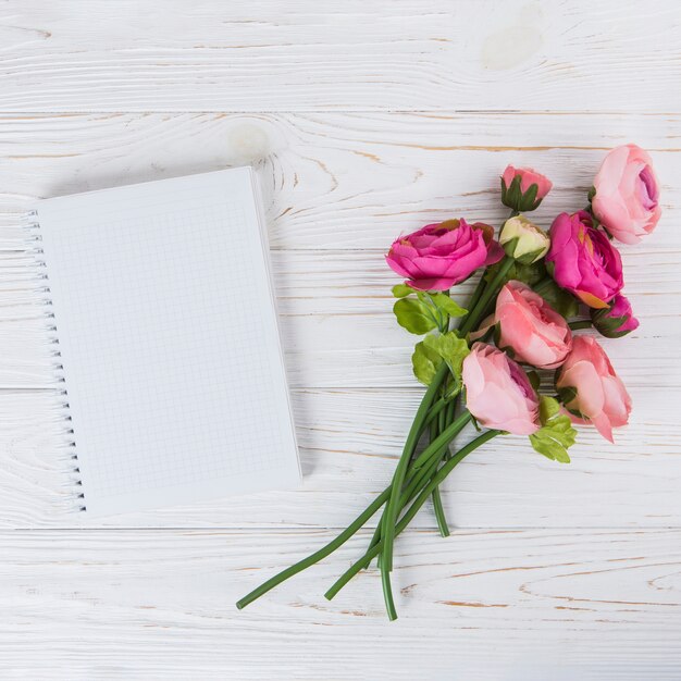 Rosa rosa flores con cuaderno en blanco en la mesa