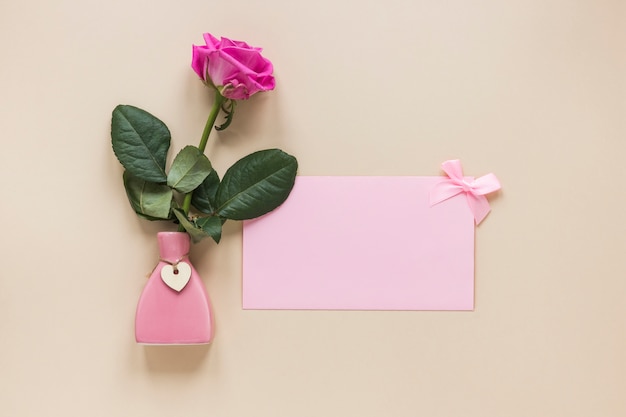 Rosa rosa en pequeño jarrón con papel sobre mesa
