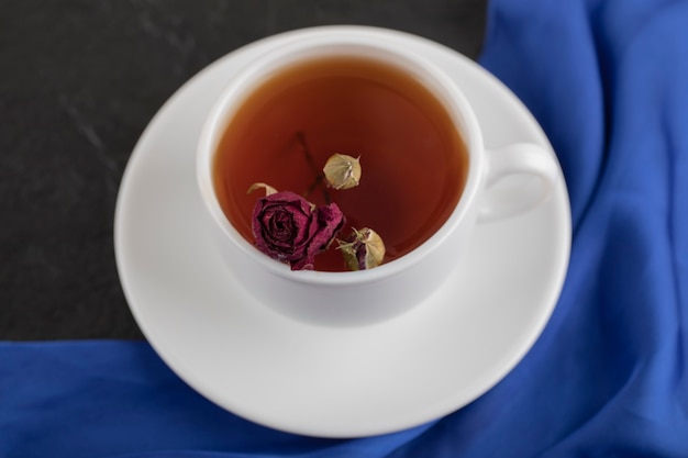 Rosa seca en una taza de té caliente sobre una mesa negra.