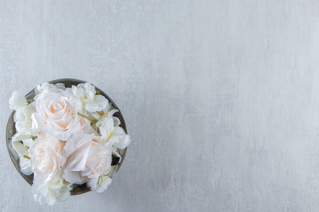 Rosas blancas en un cuenco de hierro, sobre la mesa blanca.