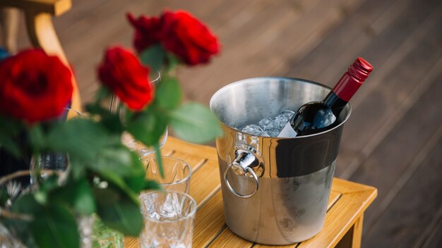 Rosas y botella de vino en el cubo de hielo en la mesa