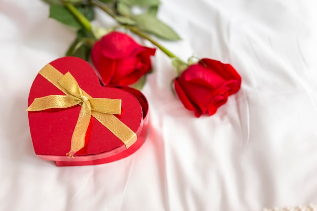 Rosas y caja de caramelos en forma de corazón en la cama