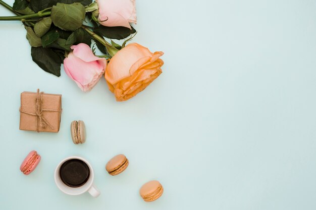 Rosas; caja de regalo; Taza de café y macarrones sobre fondo azul