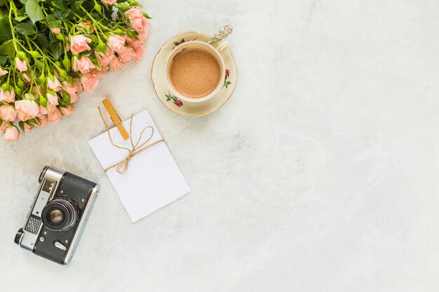 Rosas flores con taza de café; Tarjeta de felicitación y cámara vintage sobre fondo de hormigón.