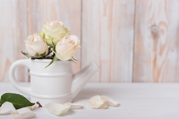 Rosas en la pequeña regadera de cerámica en el escritorio de madera.