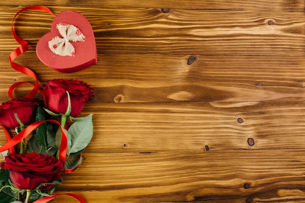 Rosas rojas con caja en forma de corazón en mesa