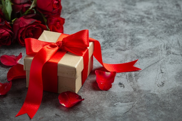 Rosas rojas y caja de regalo sobre fondo oscuro