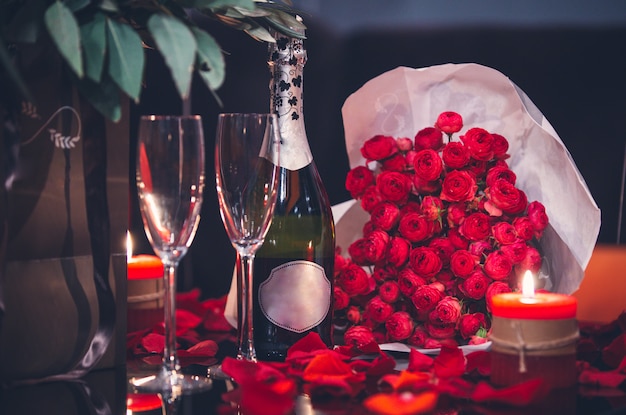 Rosas rojas, dos copas, una botella de champagne y una vela sobre la mesa.