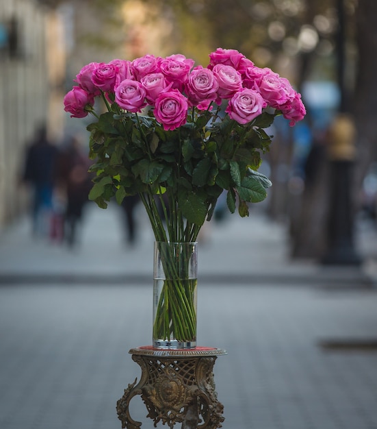 Rosas rosadas dentro de un florero de vidrio en medio de la calle