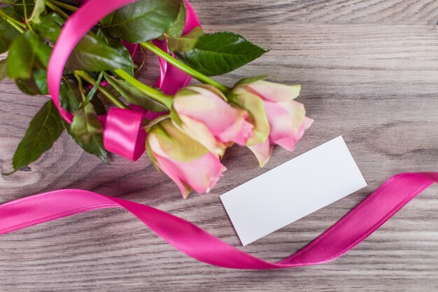 Rosas rosadas con etiqueta vacía sobre fondo de madera