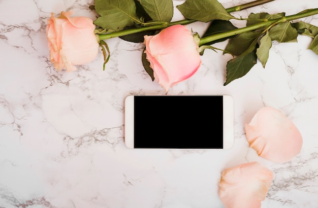 Rosas rosadas con teléfono inteligente en mármol con textura de fondo