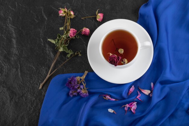 Rosas secas con una taza de té caliente sobre una mesa negra.