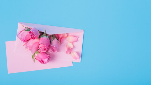 Rosas con sobre en mesa azul.