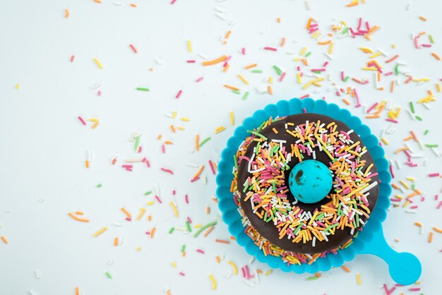 Una rosquilla de chocolate de vista superior con pequeños caramelos de colores en el escritorio blanco, dulces de color caramelo