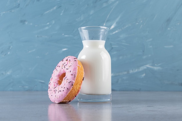 Foto gratuita una rosquilla rosa con chispitas y una jarra de vidrio con leche fresca.