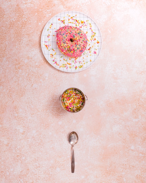 Rosquilla rosada en un plato; rociado y cuchara sobre fondo de textura rústica