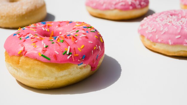 Las rosquillas rosadas con colorido asperjan en el fondo blanco