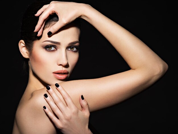 Rostro de una hermosa niña con maquillaje de moda y uñas negras posando sobre pared oscura