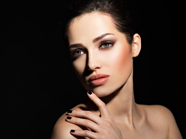 Rostro de una hermosa niña con maquillaje de moda y uñas negras posando sobre pared oscura