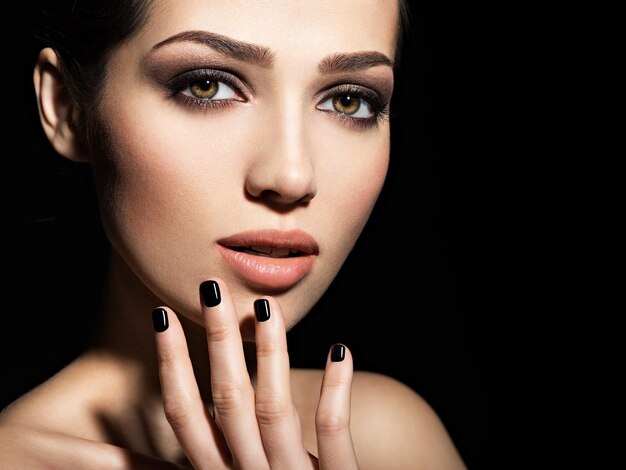 Rostro de una hermosa niña con maquillaje de moda y uñas negras posando sobre pared oscura