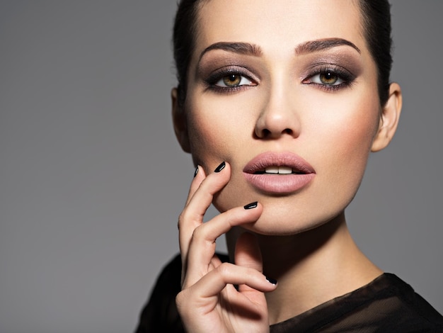 Rostro de una hermosa niña con maquillaje de moda y uñas negras posando sobre pared oscura