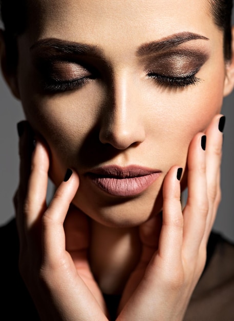 Rostro de una hermosa niña con maquillaje de moda y uñas negras posando sobre pared oscura