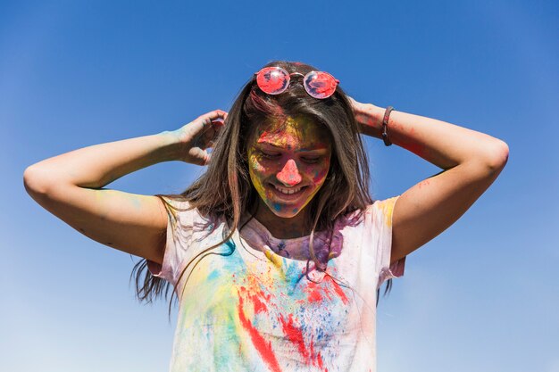 Rostro de mujer con colores holi de pie contra el cielo azul