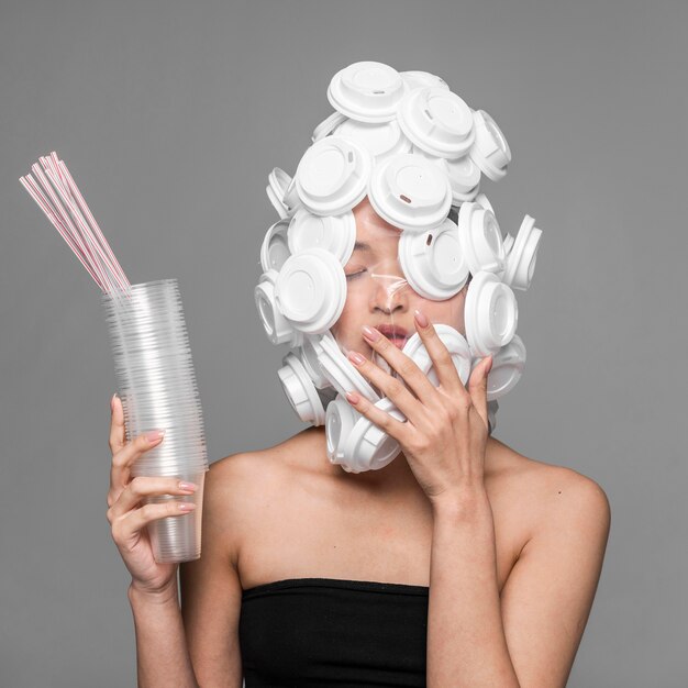 Rostro de mujer cubierto de plástico blanco y sosteniendo vasos de plástico