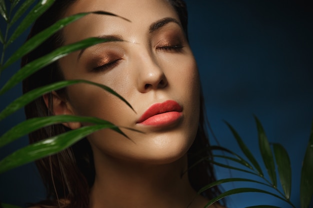 Rostro de mujer hermosa bajo exóticas hojas verdes. Fotografía de moda.