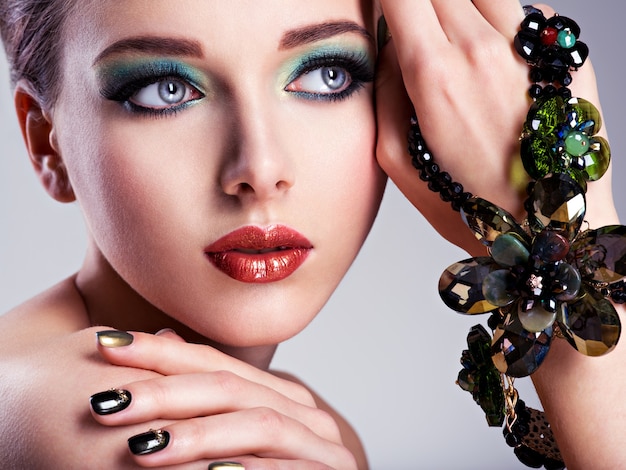 Rostro de mujer hermosa con maquillaje verde de moda y joyas a mano