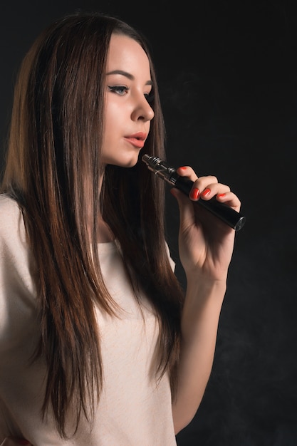 El rostro de una mujer joven vaping en el estudio negro