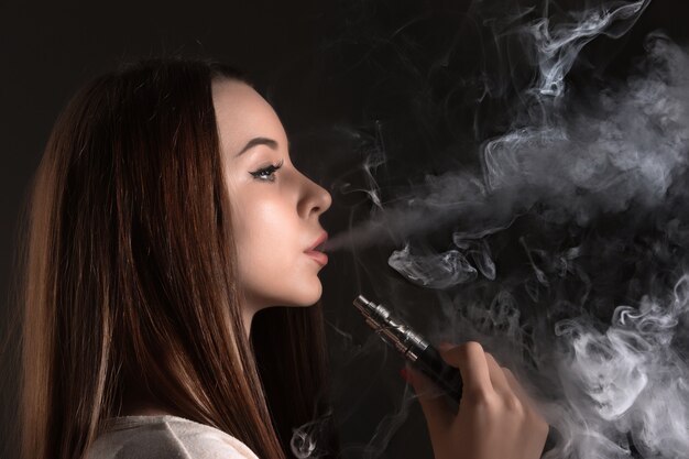 El rostro de una mujer joven vaping en el estudio negro